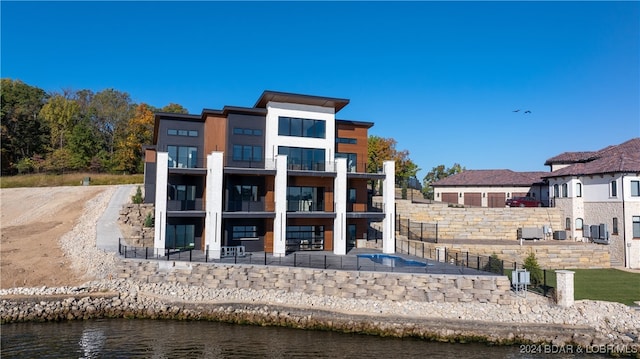 back of property with central AC unit, a water view, and a balcony