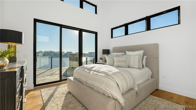 bedroom with a high ceiling, multiple windows, light hardwood / wood-style flooring, and access to outside