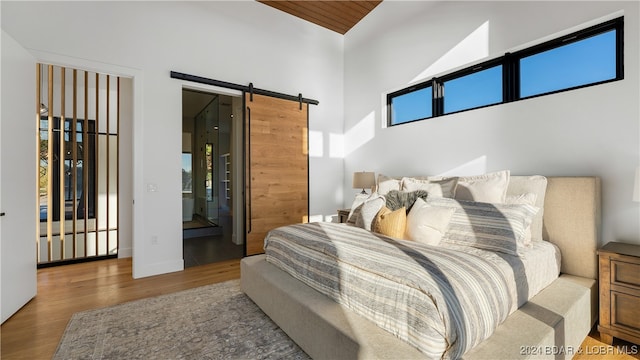 bedroom featuring high vaulted ceiling, a barn door, and hardwood / wood-style flooring