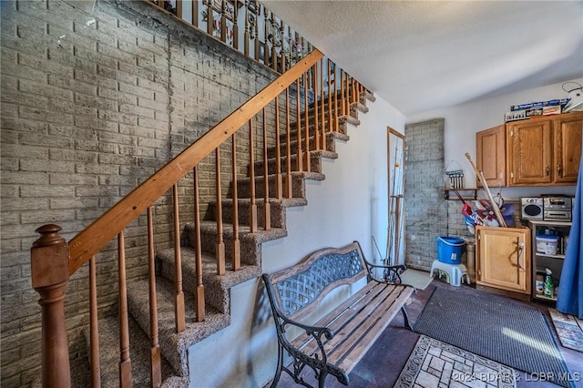 staircase featuring brick wall and a textured ceiling