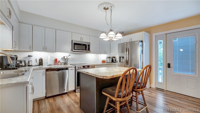 kitchen with stainless steel appliances, a kitchen island, white cabinets, and decorative light fixtures