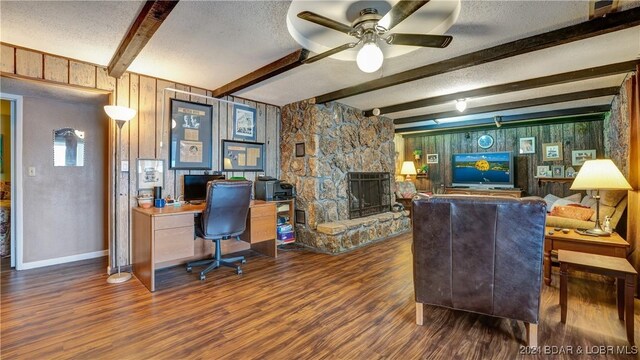 office featuring beam ceiling, a stone fireplace, dark wood-type flooring, and a textured ceiling