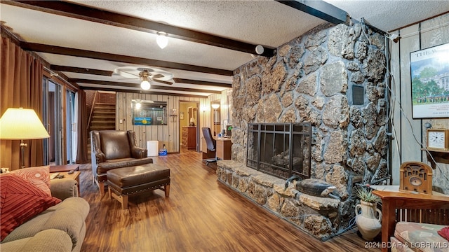 living room featuring a stone fireplace, wood-type flooring, a textured ceiling, beamed ceiling, and ceiling fan