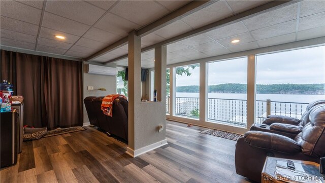 living room featuring dark hardwood / wood-style floors, a paneled ceiling, an AC wall unit, and a water view