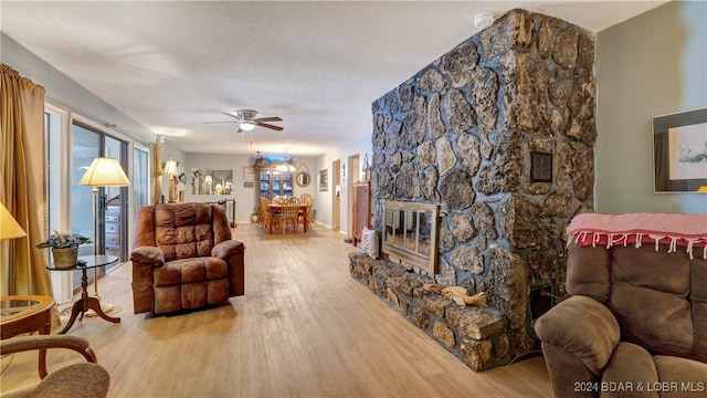 living room featuring a fireplace, ceiling fan with notable chandelier, a textured ceiling, and light wood-type flooring