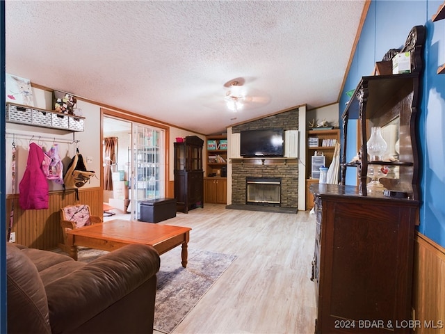 living room featuring lofted ceiling, a stone fireplace, light hardwood / wood-style flooring, ceiling fan, and a textured ceiling