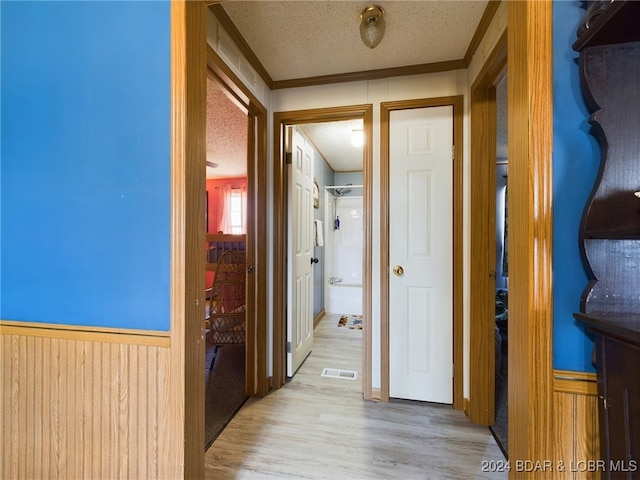 hallway featuring wood walls, ornamental molding, a textured ceiling, and light wood-type flooring