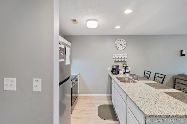 kitchen with stainless steel appliances, light wood-type flooring, light stone countertops, sink, and white cabinets