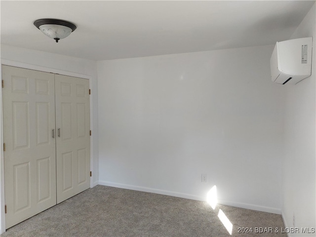 unfurnished bedroom with a wall unit AC, light colored carpet, and a closet