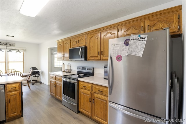 kitchen with pendant lighting, light wood-type flooring, appliances with stainless steel finishes, and a textured ceiling