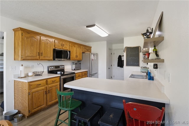 kitchen featuring stainless steel appliances, kitchen peninsula, a textured ceiling, a breakfast bar, and light hardwood / wood-style flooring