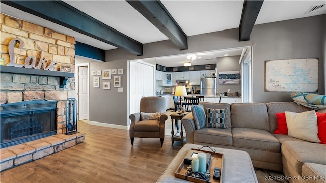 living room with a stone fireplace, light hardwood / wood-style flooring, and beamed ceiling