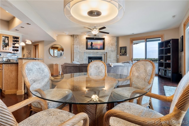 dining room with dark hardwood / wood-style flooring, a premium fireplace, ceiling fan, and bar area