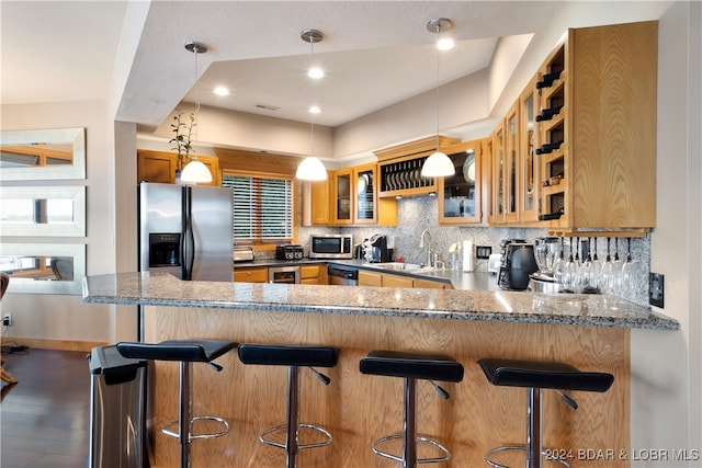 kitchen featuring a kitchen bar, sink, appliances with stainless steel finishes, kitchen peninsula, and dark stone counters