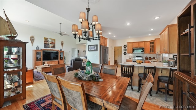 dining area with light wood-type flooring, ceiling fan with notable chandelier, and sink