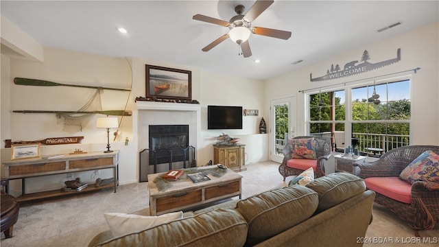 living room with a tiled fireplace, light carpet, and ceiling fan