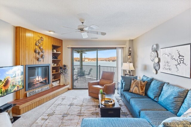 living room featuring a water view, ceiling fan, a textured ceiling, light colored carpet, and a tiled fireplace