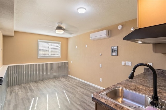 kitchen with hardwood / wood-style floors, a wall mounted air conditioner, sink, ceiling fan, and a textured ceiling