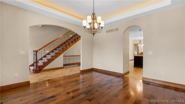 unfurnished room featuring a raised ceiling, a notable chandelier, and hardwood / wood-style floors