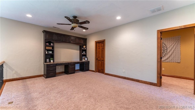 unfurnished office featuring ceiling fan, built in desk, and light colored carpet