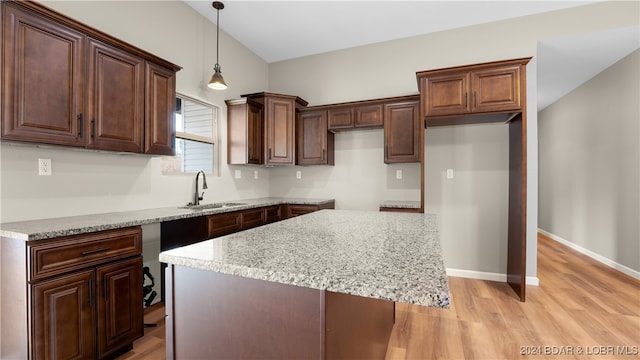 kitchen with a kitchen island, sink, light wood-type flooring, and hanging light fixtures