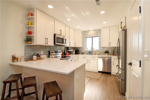 kitchen with kitchen peninsula, appliances with stainless steel finishes, light wood-type flooring, a breakfast bar, and white cabinetry