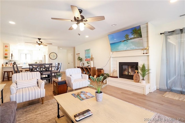 living room with ceiling fan, light wood-type flooring, and a fireplace