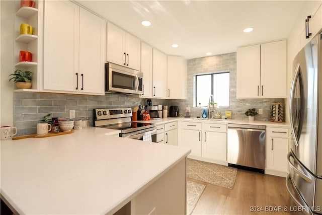 kitchen featuring white cabinetry, sink, stainless steel appliances, kitchen peninsula, and light hardwood / wood-style floors