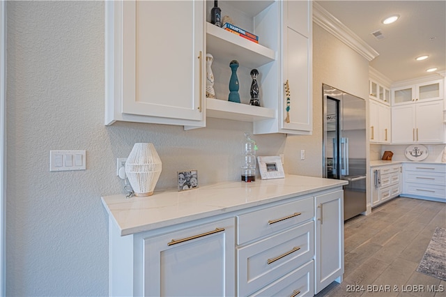 kitchen with light stone countertops, light wood-type flooring, white cabinetry, and built in refrigerator