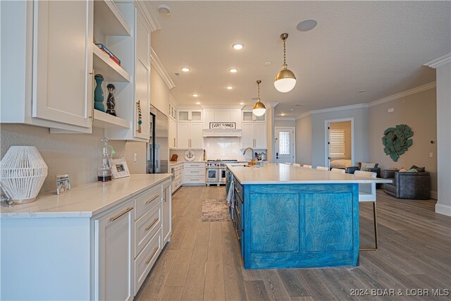 kitchen with white cabinets, decorative light fixtures, double oven range, and an island with sink