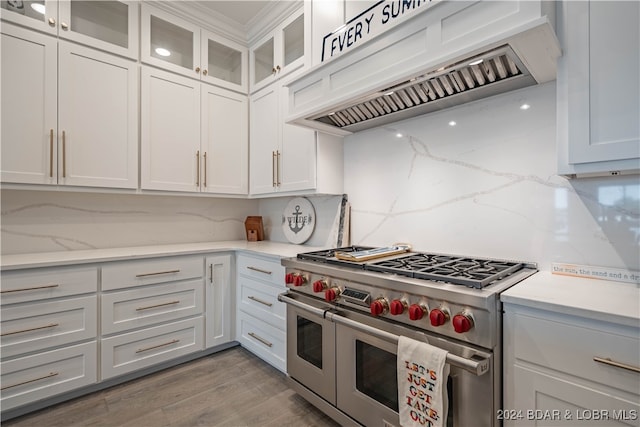 kitchen with wood-type flooring, double oven range, white cabinetry, and premium range hood