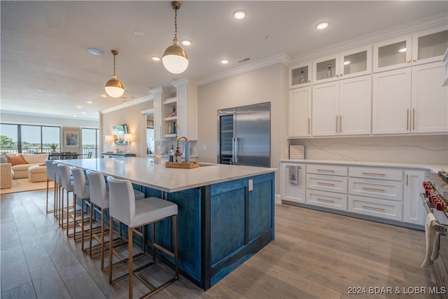 kitchen featuring light hardwood / wood-style flooring, an island with sink, appliances with stainless steel finishes, decorative light fixtures, and white cabinetry