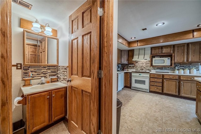 kitchen with backsplash, white appliances, sink, and wall chimney range hood