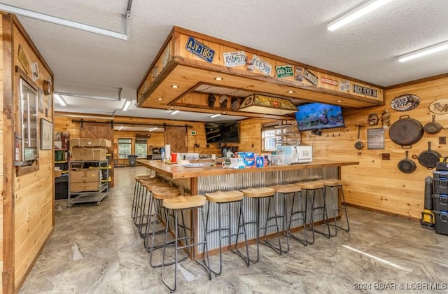 bar with butcher block counters, a textured ceiling, concrete floors, and wooden walls