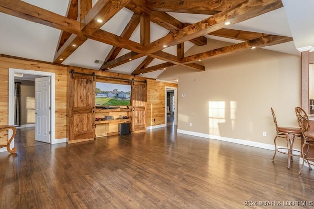 unfurnished living room featuring a barn door, beam ceiling, and wooden walls