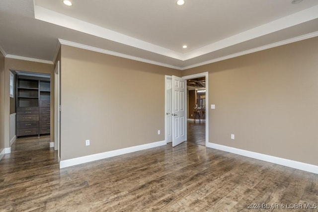 empty room featuring a raised ceiling, crown molding, dark hardwood / wood-style flooring, and built in features