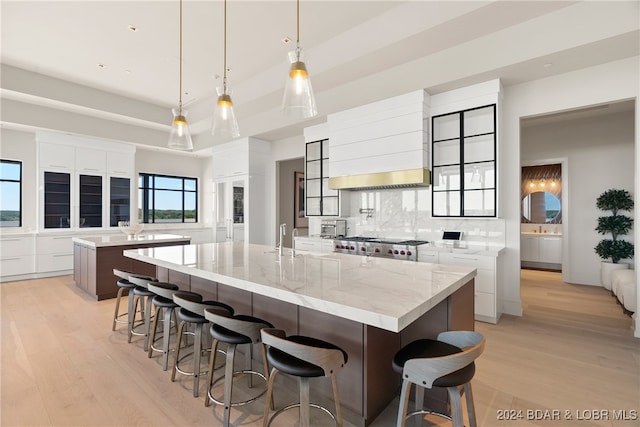 kitchen with custom range hood, light hardwood / wood-style flooring, white cabinets, hanging light fixtures, and a large island