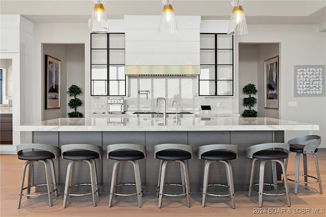 kitchen with a large island, a kitchen breakfast bar, backsplash, light hardwood / wood-style floors, and white cabinets