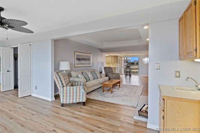 living room featuring a tray ceiling, ceiling fan, light hardwood / wood-style flooring, and sink