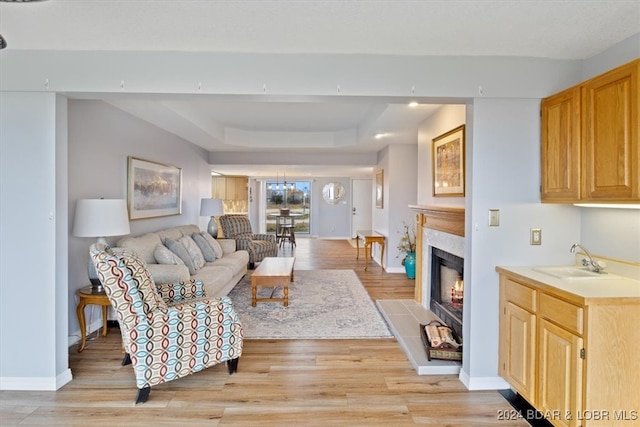 living room featuring a tray ceiling, light hardwood / wood-style flooring, and sink