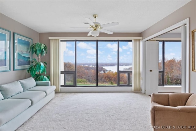 carpeted living room with ceiling fan, plenty of natural light, and a water view