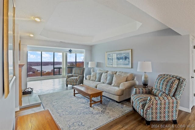 living room with light wood-type flooring, a raised ceiling, and ceiling fan