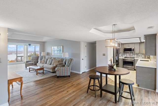 living room featuring a tray ceiling, light hardwood / wood-style flooring, a textured ceiling, and sink