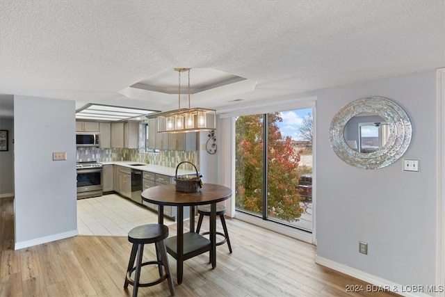 dining area with a textured ceiling, light hardwood / wood-style floors, sink, and a tray ceiling