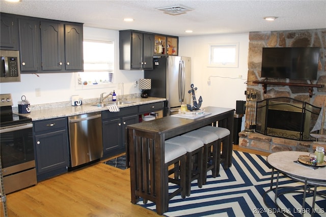 kitchen with light wood-type flooring, a textured ceiling, stainless steel appliances, and sink