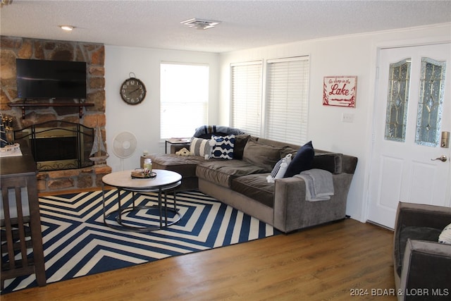 living room featuring a textured ceiling, a stone fireplace, and dark wood-type flooring