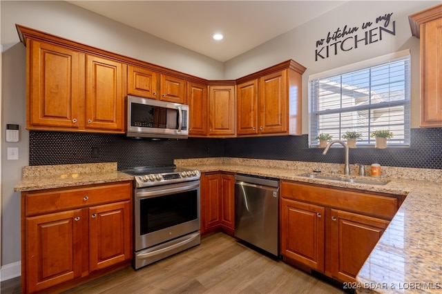 kitchen with sink, decorative backsplash, light hardwood / wood-style floors, light stone counters, and stainless steel appliances