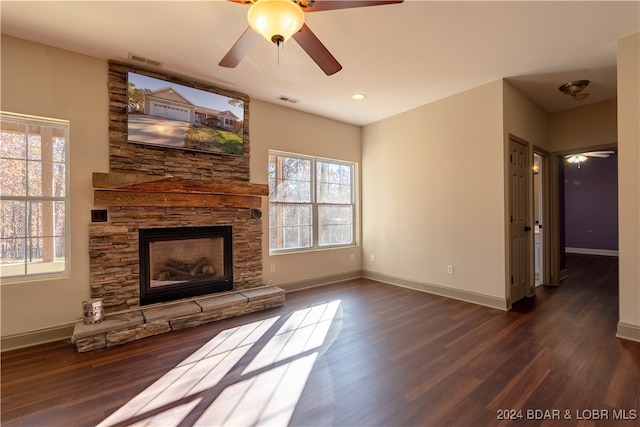 unfurnished living room with ceiling fan, a stone fireplace, and dark wood-type flooring