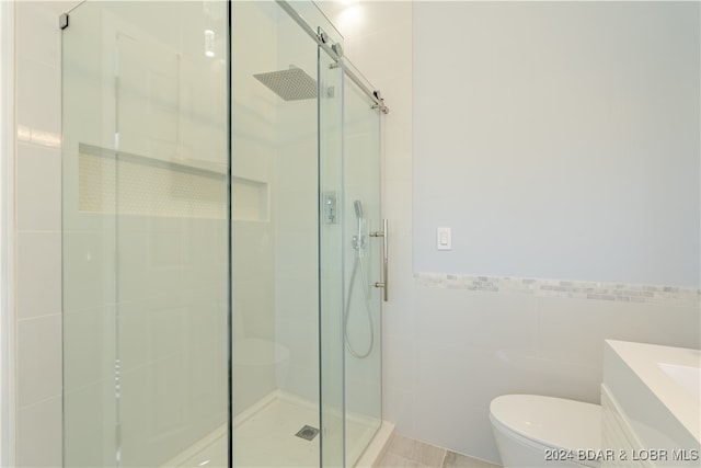 bathroom featuring walk in shower, vanity, toilet, and tile walls