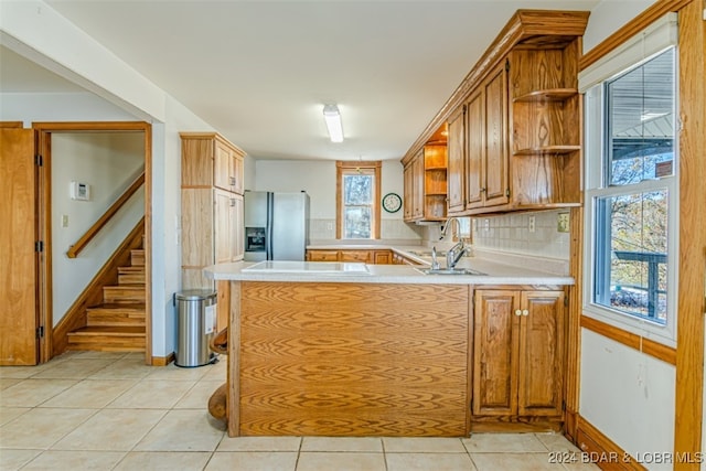 kitchen with cooktop, stainless steel fridge with ice dispenser, kitchen peninsula, decorative backsplash, and light tile patterned floors